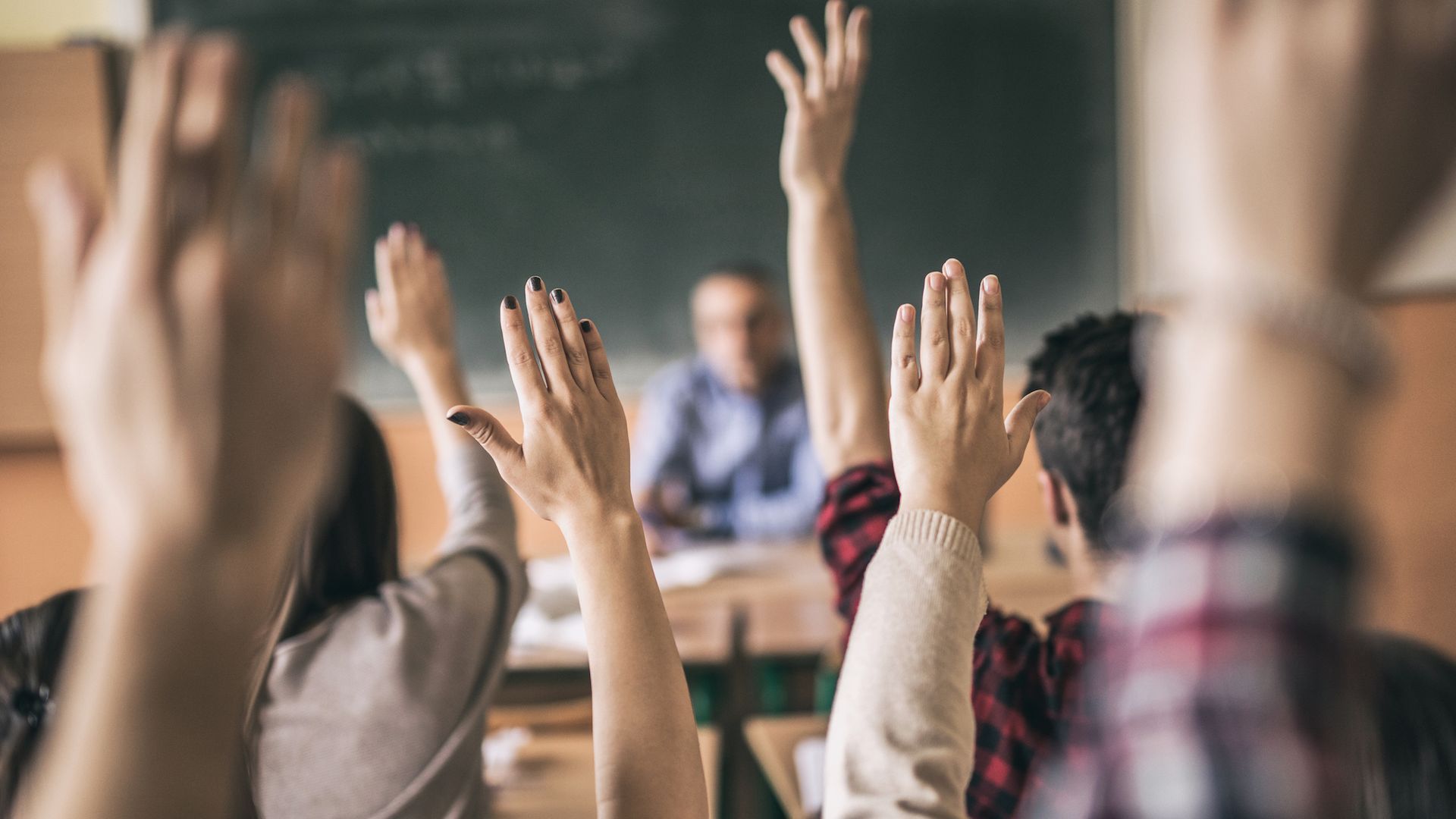 view from the back of a classroom with several students' hands raised in the air