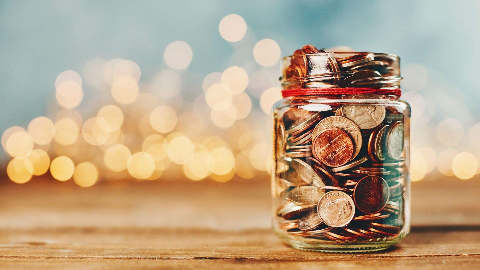 a glass jar full of coins with twinkle lights in the background