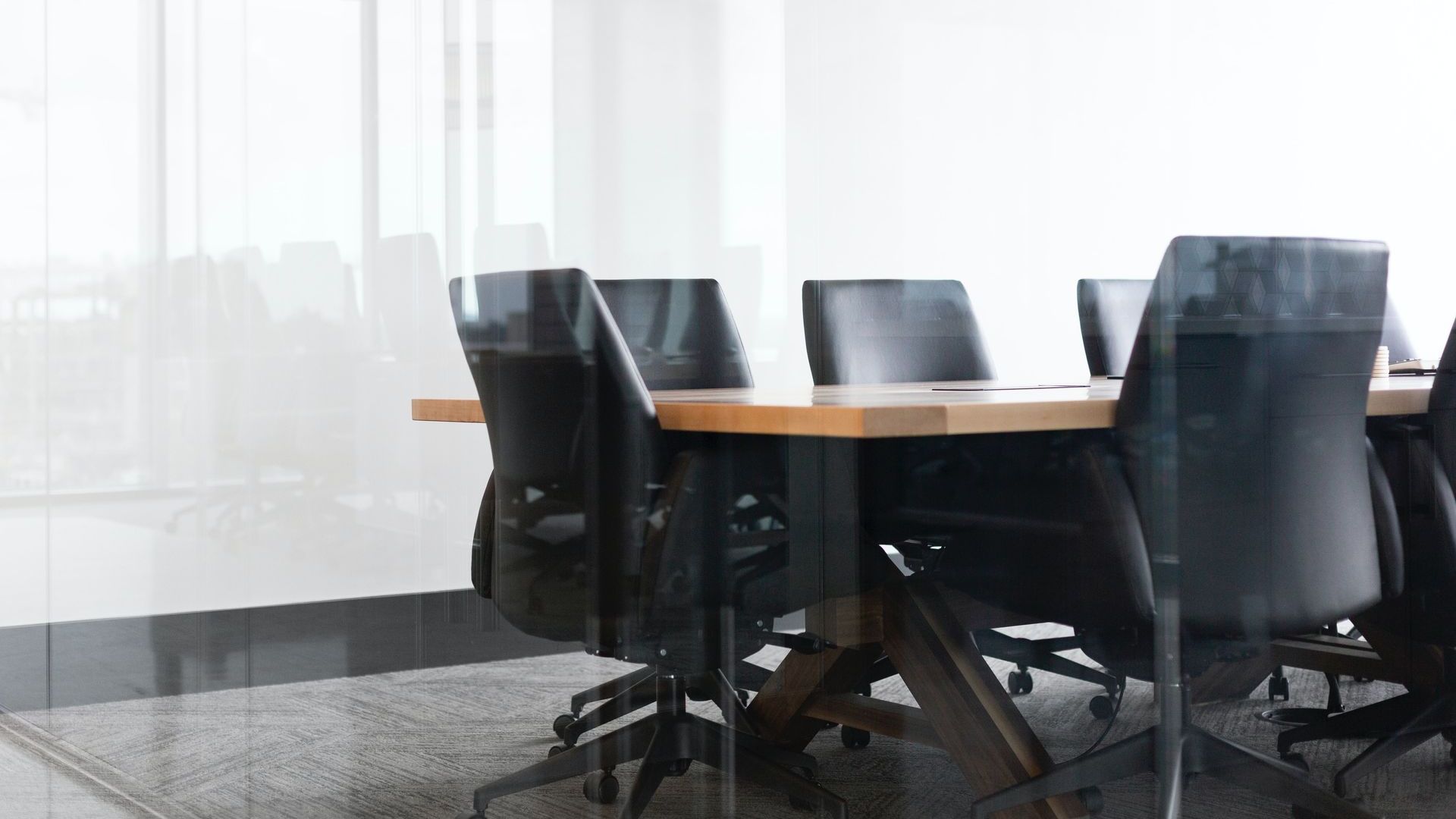 an empty conference table and black office chairs through a glass wall