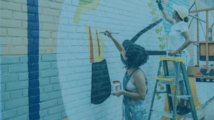 Two people painting a mural on brick wall