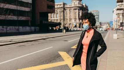 A young darker-skinned female stands on the sidewalk waiting to cross the street