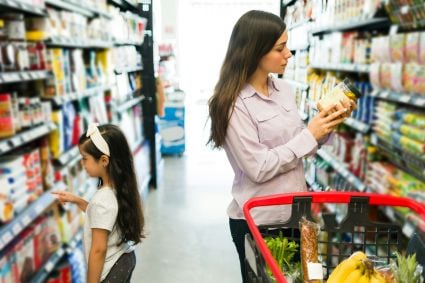 A mother and daughter standing in a grocery store aisle with a cart