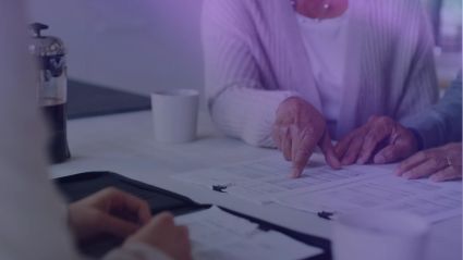 A person's finger points at a document on a desk.