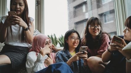 Five friends sitting together using their phones.