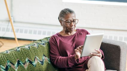 An elderly woman using a tablet while she sits on a couch.