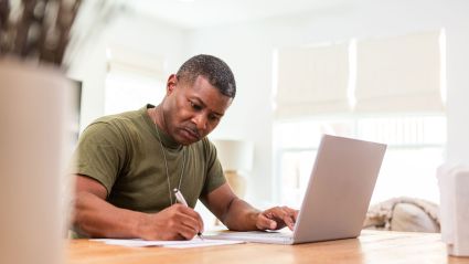 person at laptop and writing at desk