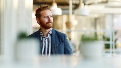 A man with red hair and beard wearing a suit looking left