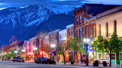 A city street with low-rise connected buildings lining the street and a snowy mountain background, leading to an article titled "The Rise of Mid-Sized American Cities: The Drivers of Perfectly-Sized Growth"