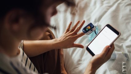 Image of a person's hands who is using a pulse oximeter and reading the results on a smart phone, acting as a hero image for an article about self-sustaining models for preventative health investments