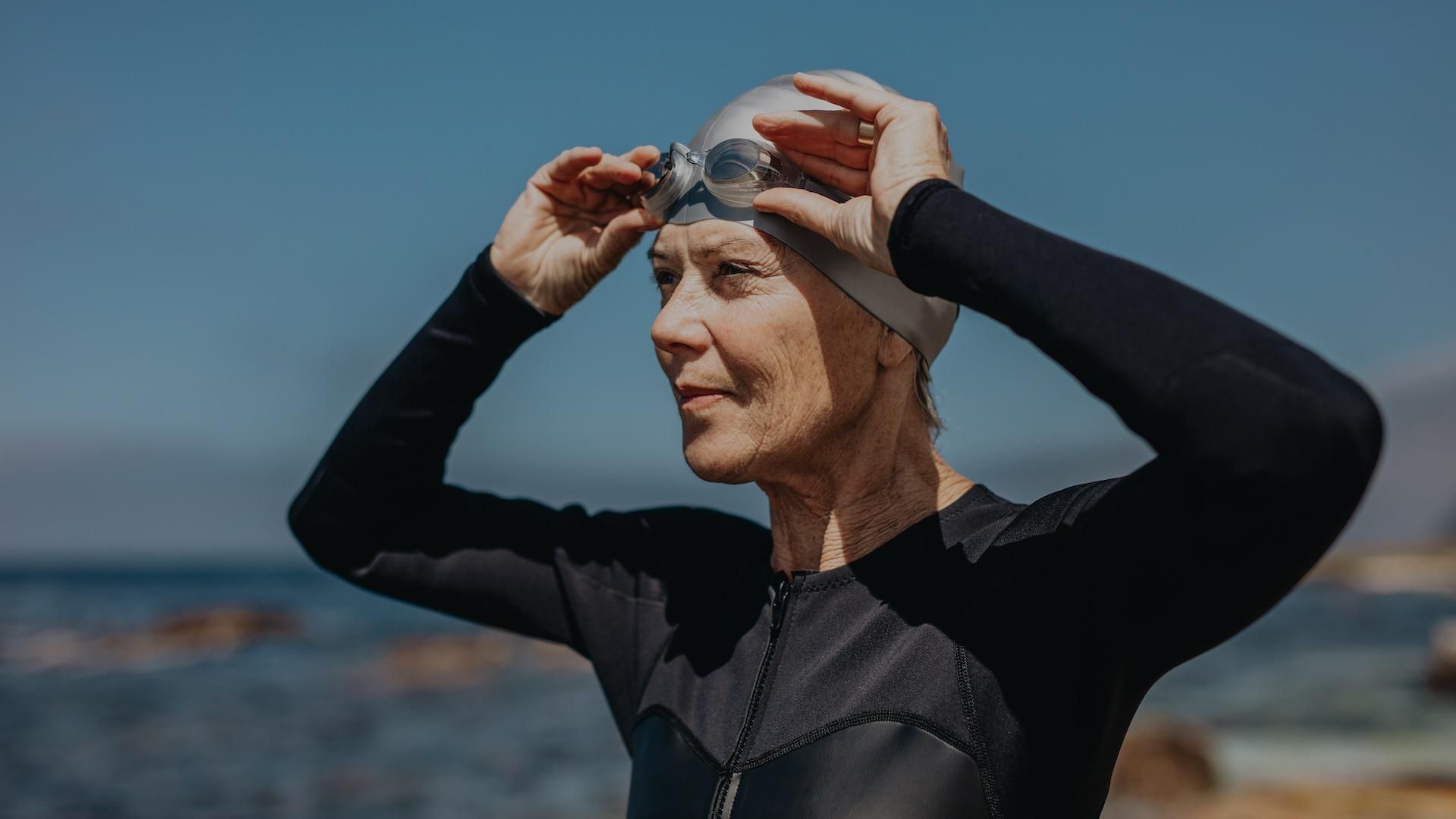 A swimmer in a wetsuit and cap adjusts their goggles while looking into the distance