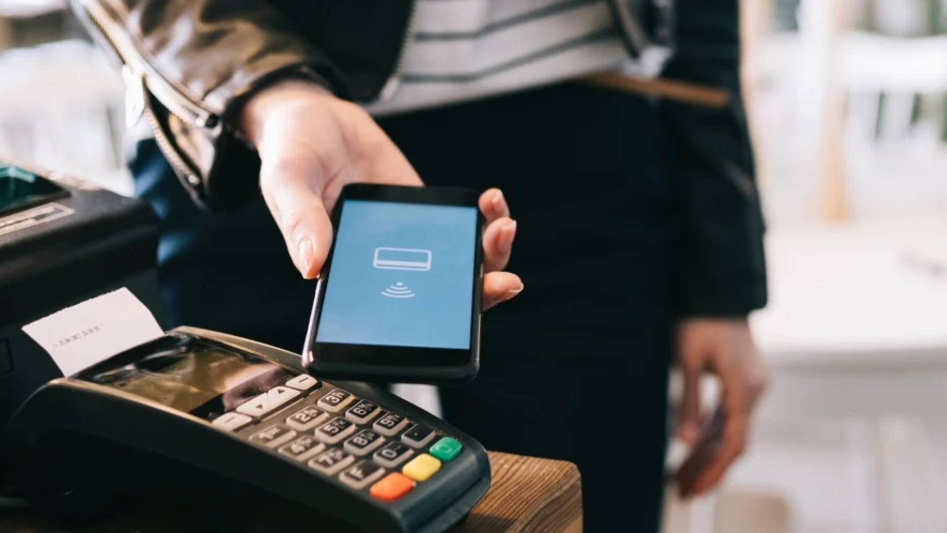 Person holds mobile phone in front of a card reader for payment