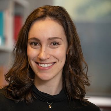 A smiling female-presenting person with brown hair against a blurred background