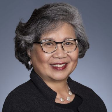 A smiling female-presenting person wearing eye glasses against a gray background.