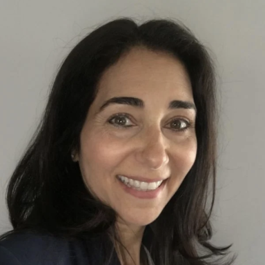 A smiling female with dark brown hair wearing a dark shirt against a light gray background