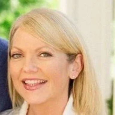 A smiling light-skinned female with blonde hair against an outdoor background