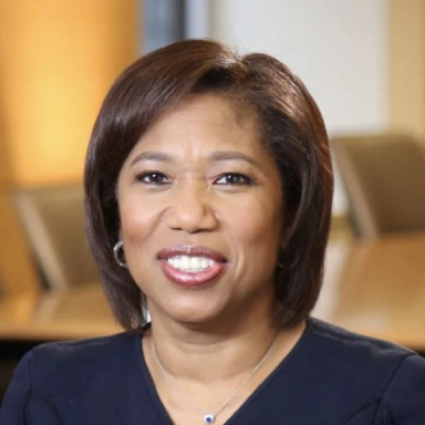 A smiling darker-skinned female with short brown hair wearing a navy shirt against an ambiguous background