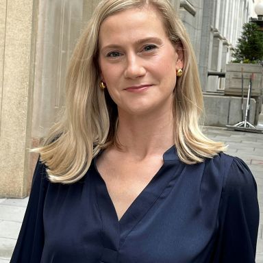 A smiling light-skinned female with blonde hair wearing a navy blue shirt against an ambiguous background