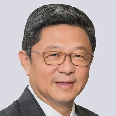 A smiling male of Asian heritage wearing glasses and a suit and tie against a white background