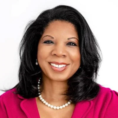 A smiling darker-skinned female with medium length black hair wearing a pink shirt against a white background