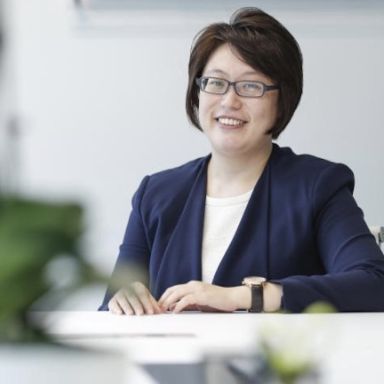 A smiling woman in an office wearing a navy blazer.