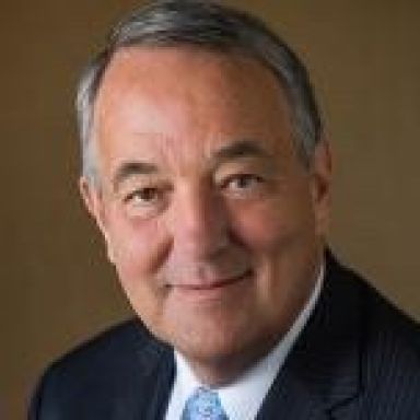 A man in a suit against a light brown background.