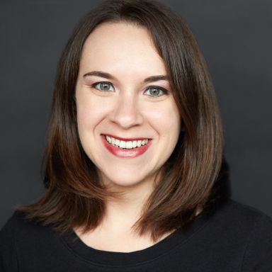 A smiling light-skinned female with short brown hair wearing a black shirt against a gray background