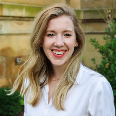 A smiling light-skinned female with long blonde hair wearing a white shirt against an outdoor backdrop