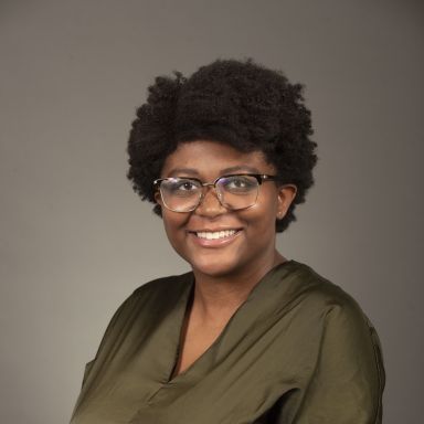 A smiling darker-skinned female with short black hair wearing a green shirt against a gray background