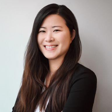 A smiling professional women wearing a black blazer against a white background,