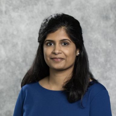 person with long dark hair pulled half back, wearing medium blue shirt, partially smiling