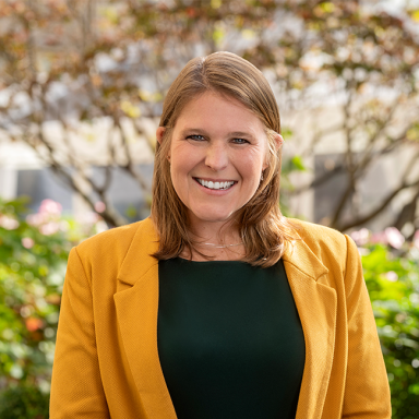 Light-skinned female-presenting person named Caitlyn Barrett with light hair in a yellow jacket and black shirt with gray gradient background