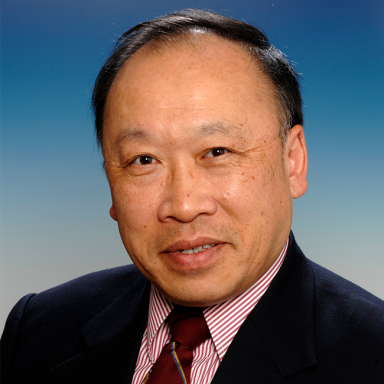 An image of an older adult man who is Asian in appearance, with short black hair and brown eyes. He is wearing a suit and tie and smiling at the camera against a blue background.