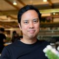 A smiling male of Asian heritage with black hair wearing a black shirt against an ambiguous background