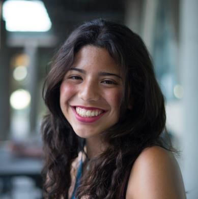 A smiling female-presenting person with dark brown hair against an open room backdrop