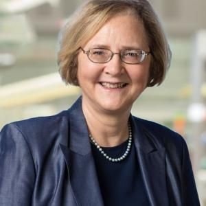 A female-presenting person with short light hair wearing a blue blazer against a blurred background.