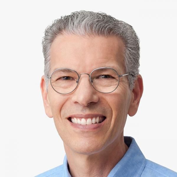 A light-skinned male-presenting person with short, gray hair and glasses wearing a blue shirt against a white background