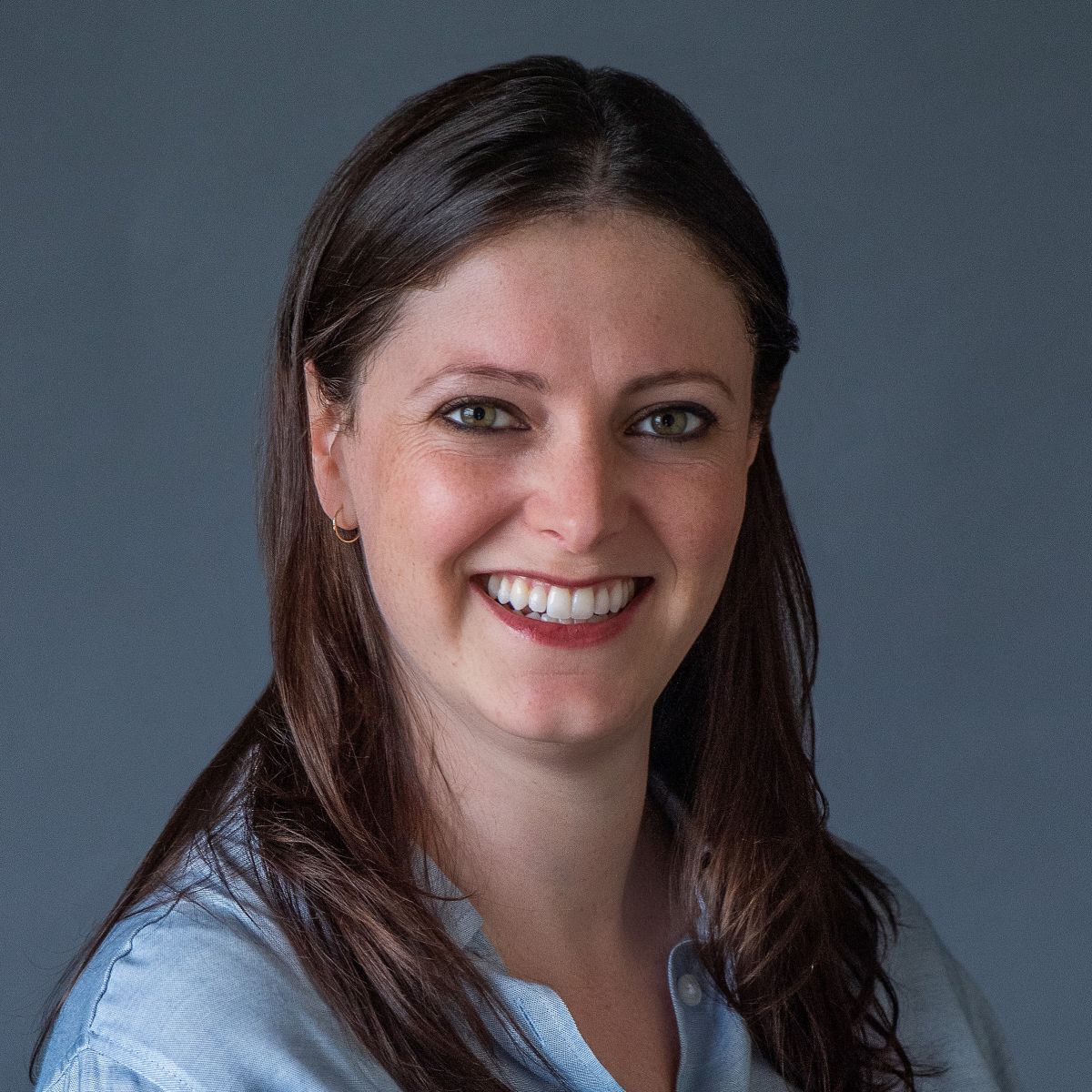 Smiling female-presenting individual with dark brown hair against a gray background