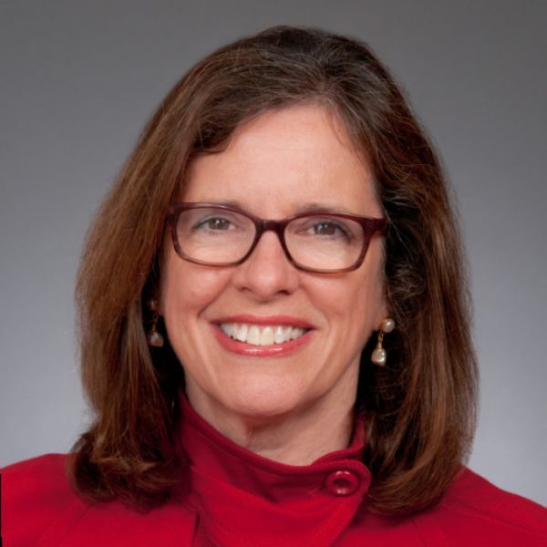 Smiling medium-skinned, female-presenting individual with medium length dark hair wearing a red shirt on a grey backdrop