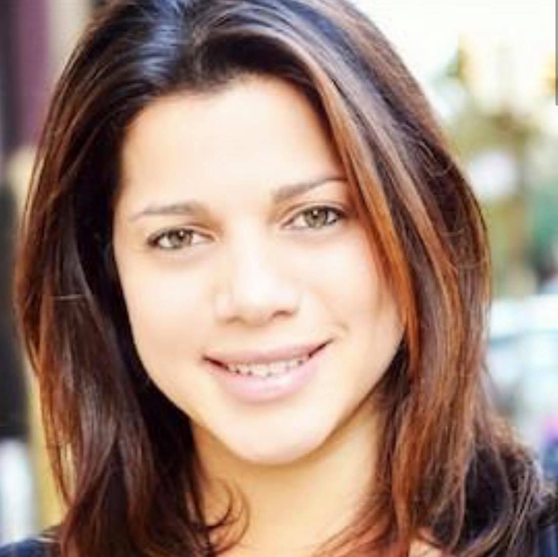 Smiling person, presenting as female, with brown hair with an outdoor background