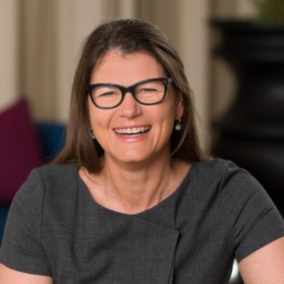 Smiling light-skinned, female-presenting individual with long dark hair wearing a dark shirt on a brown backdrop.