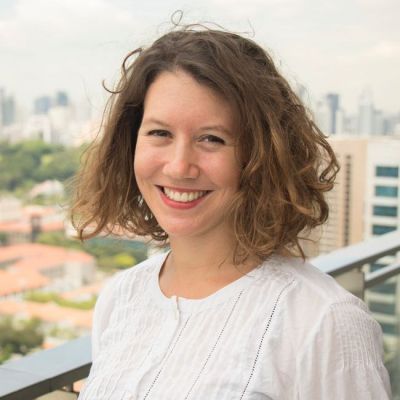 Smiling light-skinned, female-presenting individual with medium length brown hair wearing a white shirt outdoors