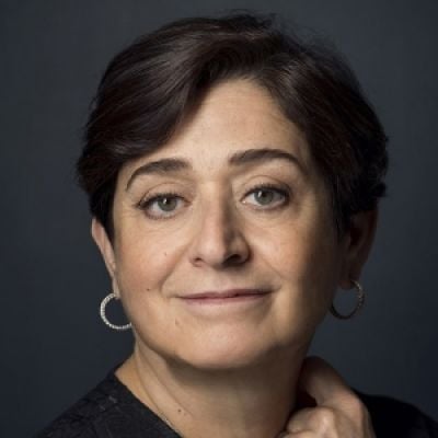 Smiling light-skinned, female-presenting individual with short dark hair wearing a dark shirt on a brown backdrop.