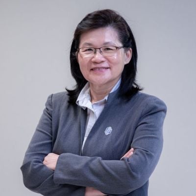 Smiling female-presenting individual with long dark hair wearing a grey suit on a grey backdrop.