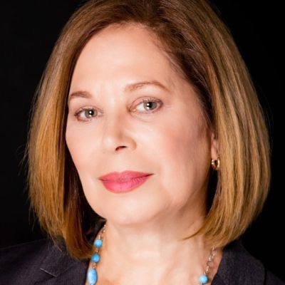 A female-presenting person with short brown hair wearing a dark suit against a dark background