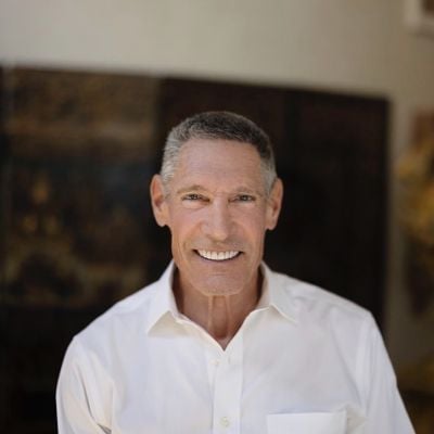 Smiling light-skinned, male-presenting individual with short grey hair wearing a white shirt