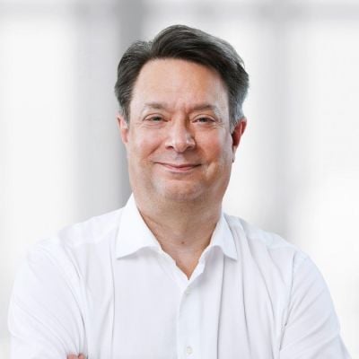 A smiling light-skinned male with dark brown hair wearing a white button-up against a light gray and white background