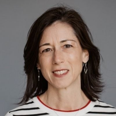 A smiling light-skinned female with short dark brown hair wearing a black and white striped shirt against a gray background