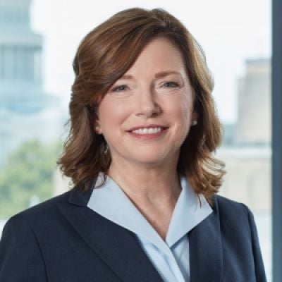 A smiling female-presenting light-skinned person with brown hair wearing a dark blue suit against an ambigious background