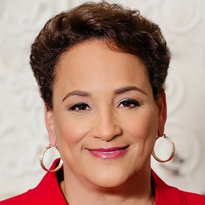 A smiling medium-skinned female with short dark brown hair wearing a red jacket against a white background