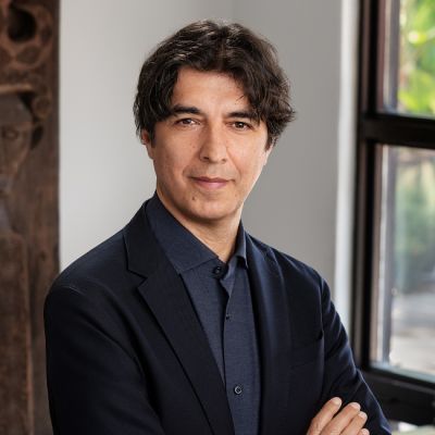 A light-skinned male with dark brown hair wearing a navy shirt under a black suit jacket against an ambiguous backdrop